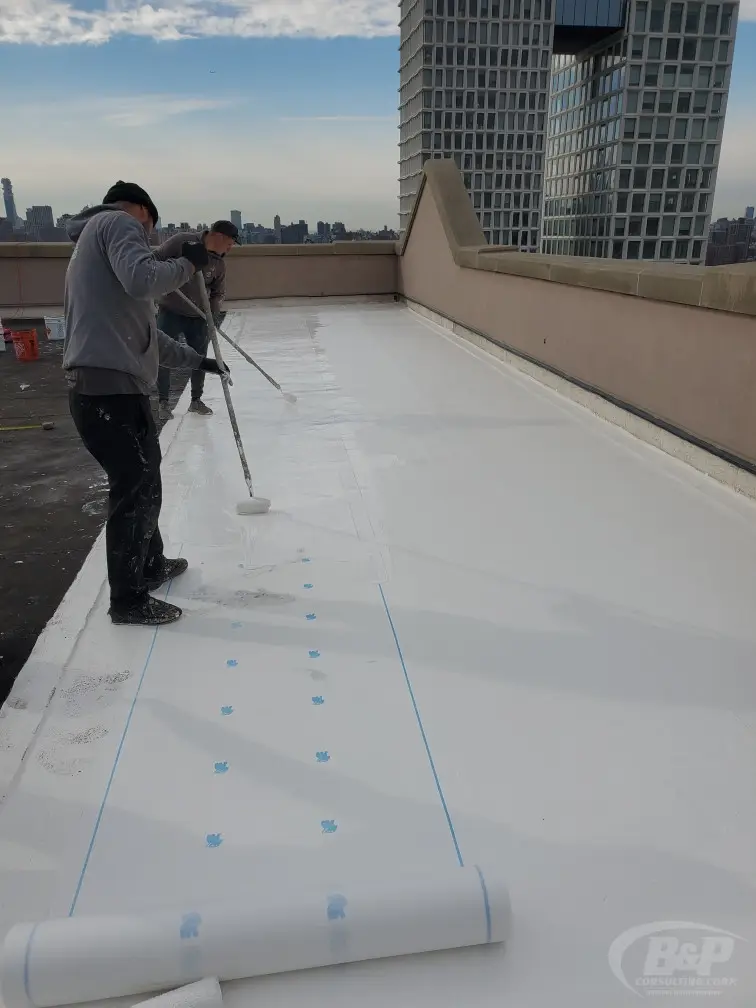 A B&P crew member rolling a liquid-applied waterproofing membrane onto a flat roof