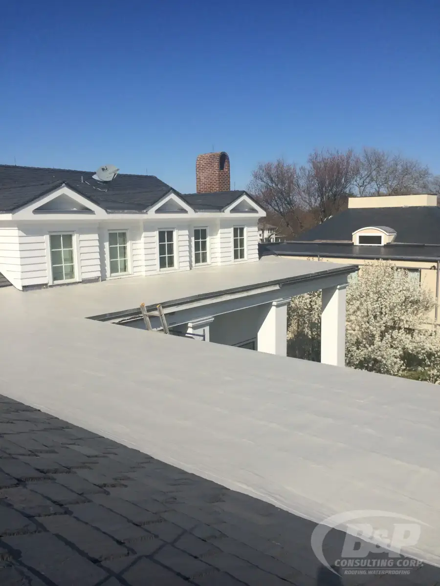 Sloped slate roof meeting a new flat roof section on a white house